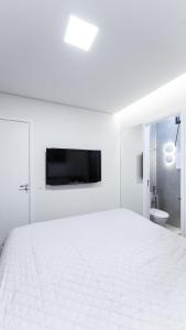 a white bedroom with a large bed and a tv on the wall at Apartamento Duplex de luxo em Campos do Jordão in Campos do Jordão