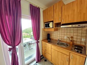 a kitchen with purple curtains and a sink and a window at Apartment Tomić 3 Makarska in Makarska