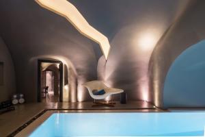 a room with a white chair and a swimming pool at Kivotos Santorini - Preferred Hotels & Resorts in Imerovigli +38 photos