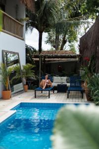 a man sitting on a chair next to a swimming pool at Pousada Bem Te Vi Trancoso in Trancoso