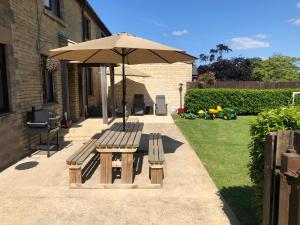 un banco de madera y una sombrilla en un patio en Moo Cow Cottage Self Catering, en Oakham