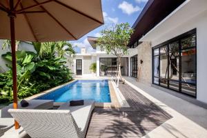 an outdoor swimming pool with chairs and an umbrella at Billi Bali Villa in Canggu