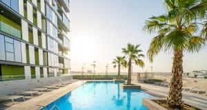 a swimming pool with palm trees in front of a building at Nasma Luxury Stays - Colorful Condo With Wide City Views From Balcony in Dubai