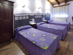 Habitación con 3 camas con sábanas moradas. en Casa Rural Sierra de Tabanera en San Andrés de Soria