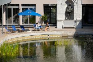 two people sitting under an umbrella next to a pond at Van der Valk Hotel Mechelen in Mechelen
