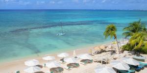 una playa con sombrillas y un barco en el agua en South Bay Beach Club - Three Bedroom Beachfront Condos by Grand Cayman Villas & Condos, en West Bay