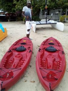 a man standing next to two red kayaks on the beach at Seacret Studios - Cozy Jamaican Retreat apts in Negril