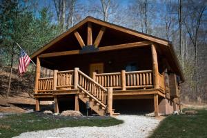 a log cabin with a porch and an american flag at Lake View Cozy Cabin Hocking Hills with Pond and Hot Tub in Rockbridge