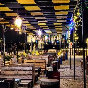 a patio with wooden tables and lights at night at Wadi Al-Wala View Camp in Madaba