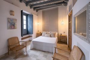a bedroom with a white bed and a chair at Casa del Museo - Agua in Medina Sidonia