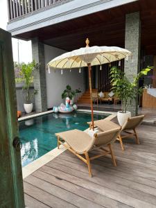 Un patio con dos sillas y una sombrilla junto a una piscina. en Tropical Beach House Bali, en Seminyak