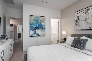 a white bedroom with a white bed and a painting on the wall at Dahlia - The Designer Townhome in Lake Worth