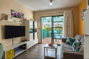 uma sala de estar com uma televisão e um sofá em Bungalow DUNA FLOR VERDE Maspalomas em Maspalomas