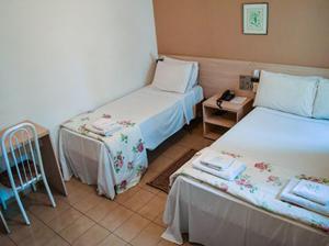 a hotel room with two beds and a table at Hotel Nações in Presidente Prudente