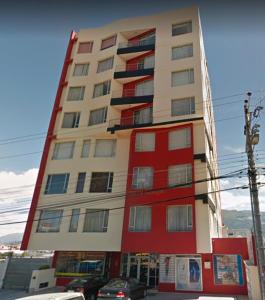 un grand bâtiment rouge et blanc avec des voitures garées devant lui dans l'établissement Departamento Privado una habitación y balcón Sector Solca y Embajada EEUU, à Quito