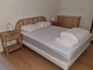 Una cama con sábanas blancas y una mesita de noche junto a un bedsenalsenalsenal en maison de village en Saint-Laurent-de-Carnols