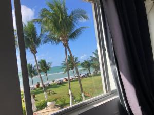 a window with a view of the ocean and palm trees at Praia dos Carneiros apart beira-mar in Tamandaré