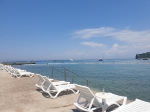 una fila de sillas y mesas blancas en una playa en Seafront Apartment Strunjan, en Strunjan