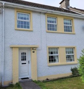 uma casa branca com janelas amarelas e uma porta em Teach pádraig em Falcarragh