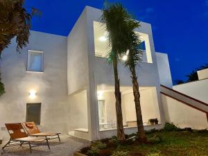 una casa blanca con una palmera y una silla en Appartamento SOLE in Villa Giulia sul Mare en Marausa