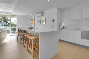 una cucina con mobili bianchi e un bar con sgabelli di The Cove Noosa - Apartment 21 a Noosa Heads