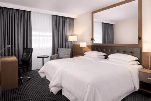a hotel room with a large white bed and a mirror at Sheraton Heathrow Hotel in Hillingdon