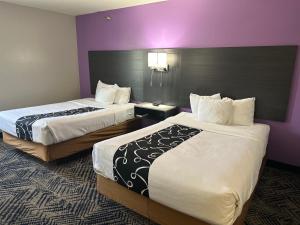 La Quinta Inn by Wyndham Omaha Southwest في أوماها: سريرين في غرفة الفندق بجدران أرجوانية