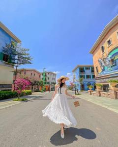 Una mujer con un vestido blanco y sombrero caminando por una calle en Khách sạn Chìa Khóa Vàng - Miễn phí tour xe điện tham quan Địa Trung Hải - TT Hoàng Hôn, en Phu Quoc