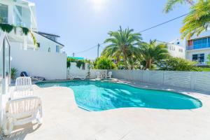 a swimming pool with two chairs and a white house at Beach Palms Holiday Apartments in Gold Coast