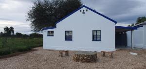 a white house with a barrel and two benches at Karoo Leeu Cottage in Oudtshoorn