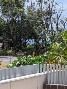 a white fence next to a street with trees at Bateau Bay Retreat in Bateau Bay