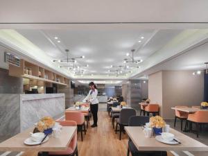 a woman standing in a restaurant with tables and chairs at Kyriad Marvelous Hotel Suzhou Wujiang People Square in Suzhou