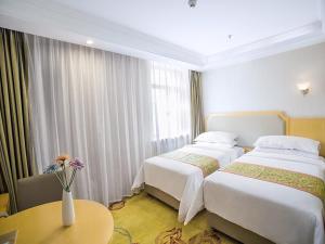 2 Betten in einem Hotelzimmer mit einer Blumenvase in der Unterkunft Vienna Hotel Harbin Train Station Jianguo Street in Harbin