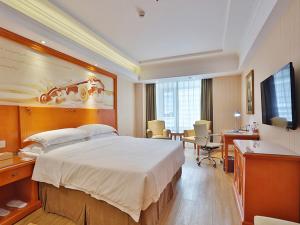 una camera d'albergo con un grande letto e una scrivania di Vienna Hotel Harbin West Railway Station Wanda Plaza a Harbin