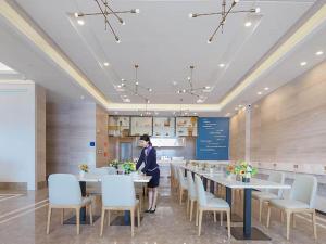 a woman standing at a long table in a restaurant at Kyriad Marvelous Hotel Huizhou Boluo Longxi in Boluo