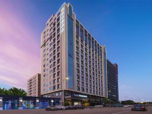 a tall building with cars parked in a parking lot at Kyriad Hotel Dongguan Houjie Convention and Exhibition Center Humen Station in Dongguan