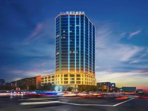 a tall glass building with cars in front of it at Kyriad Marvelous Hotel Henan Xinyang Pingqiao Plaza in Xinyang