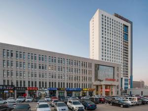 un grand bâtiment avec des voitures garées dans un parking dans l'établissement Vienna International Hotel Mongolia Chifeng High-Speed Railway Station, à Chifeng