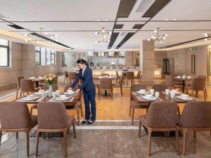 a woman standing at a table in a restaurant at Kyriad Marvelous Hotel Shenzhen Baoan Gushu Metro Station in Bao'an