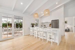 una cocina blanca con barra con taburetes en Backbeach House - relaxing coastal escape, en Blairgowrie
