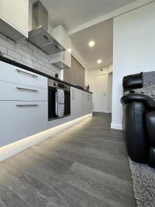 a kitchen with white cabinets and a black couch at Cozzzy Seaside Retreat in Mablethorpe