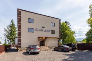 a building with two cars parked in a parking lot at Комплекс СільДар in Solotvyno