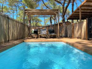 a swimming pool in a backyard with a wooden fence and a pergola at Camping la Tamarissière in Agde