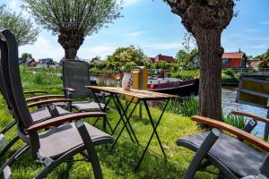 een picknicktafel en stoelen naast een rivier met een boot bij Loft in romantische stolpboerderij bij duingebied. in Warmenhuizen