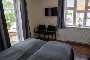 a bedroom with a bed and two chairs and windows at Nordgården Pension in Onsbjerg