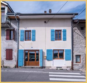 un bâtiment blanc avec volets bleus dans une rue dans l'établissement Maison de village T4 3 chambres avec parking gratuit Monnetier-Mornex, à Monnetier-Mornex