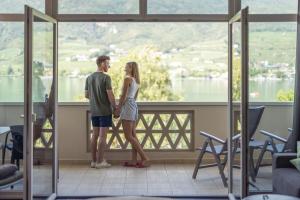 Ein Mann und eine Frau stehen auf einem Balkon mit Blick aus dem Fenster in der Unterkunft Parc Hotel Am See in Kaltern