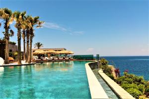 a swimming pool with palm trees and the ocean at Ala Suites and Villas Yalıkavak in Yalıkavak