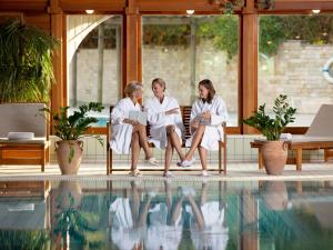 Tres mujeres con batas blancas sentadas junto a una piscina en Hotel Carbona Thermal Spa, en Hévíz