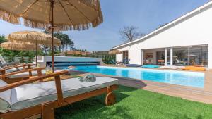 a pool with chairs and umbrellas next to a house at Villa Hakuna Matata - 4 étoiles climatisée avec piscine in Saint-Médard-en-Jalles